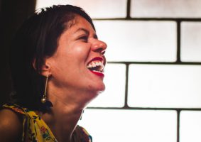 Dia Nacional da pessoa com deficiência. Fatine Oliveira, mestre em Comunicação Social e integrante do Grupo Afetos - Grupo de Pesquisa em Comunicação, Acessibilidade e Vulnerabilidades, UFMG, está de perefil, cabeça levemente levantada e sorriso contagiante. Ela é morena e tem cabelos curtos. Fatine é feminista e pessoa com deficência.