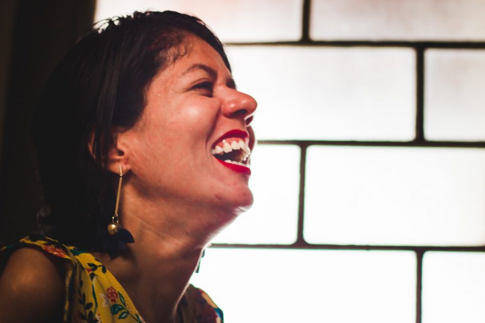 Dia Nacional da pessoa com deficiência. Fatine Oliveira, mestre em Comunicação Social e integrante do Grupo Afetos - Grupo de Pesquisa em Comunicação, Acessibilidade e Vulnerabilidades, UFMG, está de perefil, cabeça levemente levantada e sorriso contagiante. Ela é morena e tem cabelos curtos. Fatine é feminista e pessoa com deficência.